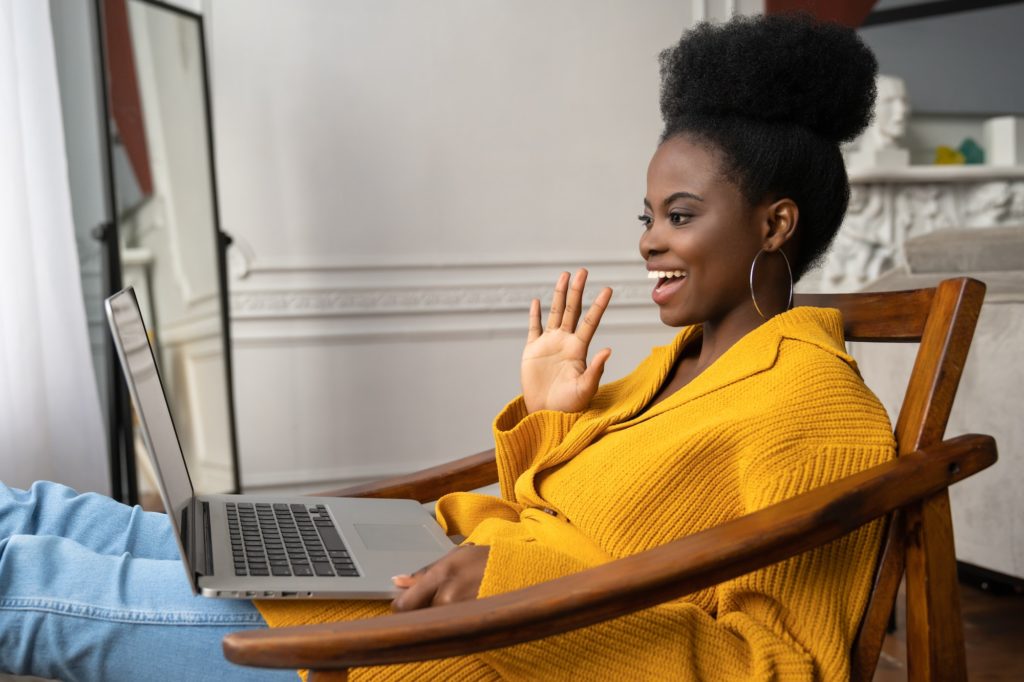 Smiling African American biracial millennial woman talking in video chat with her friends, say hello